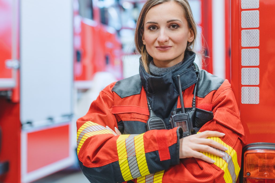 Fire fighter woman standing in front of a fire truck with her arms crossed
