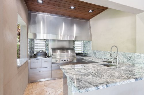 Beautiful luxury outdoor kitchen with all accessories, grill, stove, sink, green marble countertop, industrial extractor fan, wooden roof