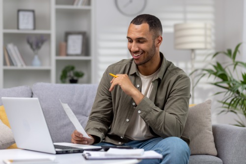 Man at home sitting on sofa in living room, calculating and paying bills, man with calculator and laptop online paying for rent and loan.