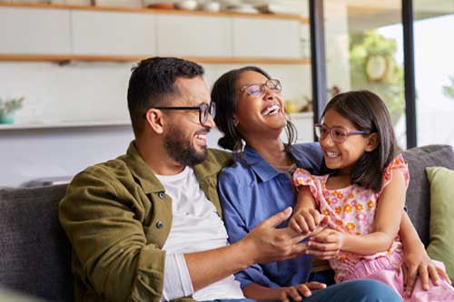 Cheerful middle eastern family with eyeglasses of three having fun together at home. Mixed race parents talking with their little girl in living room. Cheerful family with specs embracing and playing.