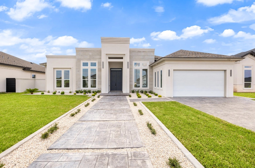 Modern single-story home with a landscaped front yard, stone pathway, and a two-car garage under a blue sky.
