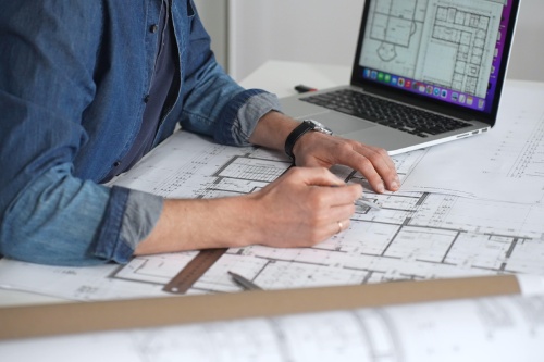 Architect drawing and measuring blueprints on a desk, creating detailed floor plans and designs for construction projects, demonstrating precision and expertise in architectural planning