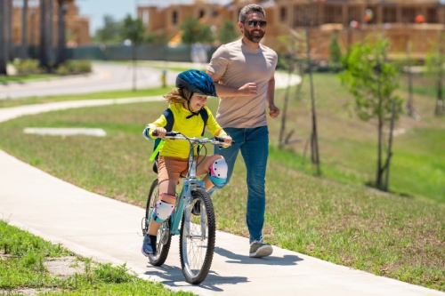 Father and son learning to ride a bicycle having fun together at Fathers day. Father teaching his son cycling on bike in american neighborhood. Father and son concept. Father